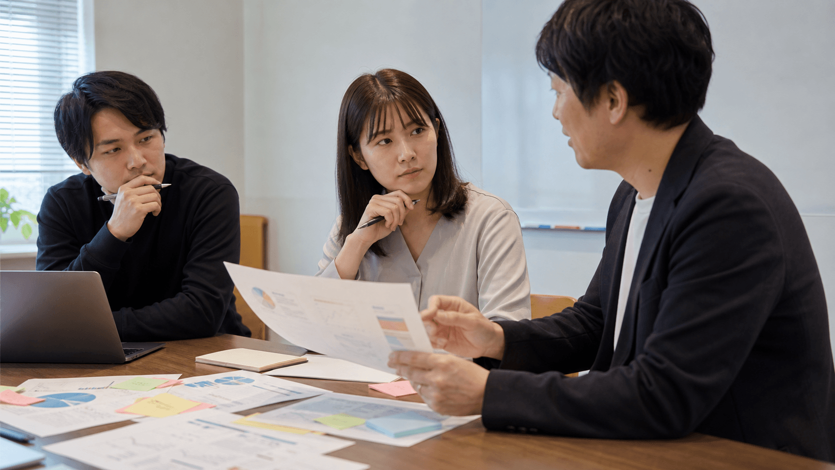 地方企業の研修担当者と現場リーダーが、研修資料と付箋を見ながら生成AI研修後の質問対応フローを話し合っている様子