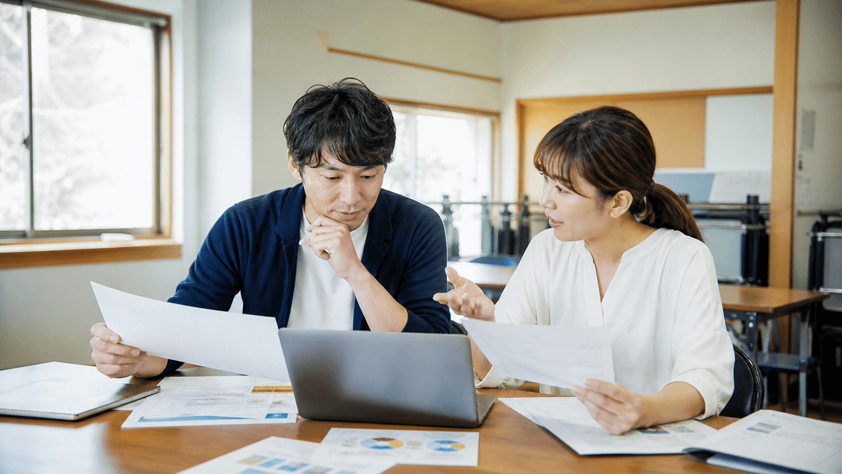 地域の教室で、主催者2人がノートPCと印刷した案内資料を見ながら、子ども向け生成AI体験会の保護者向け説明内容を確認している様子