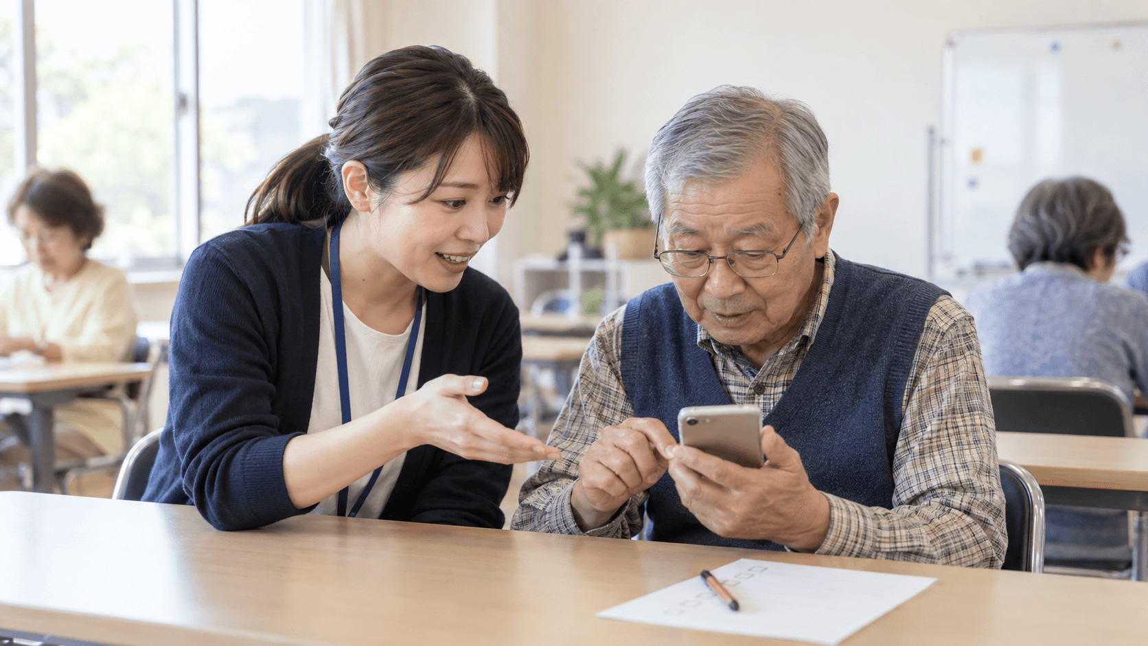 地域のスマホ教室で、講師が参加者本人のスマートフォン操作を横から説明している様子