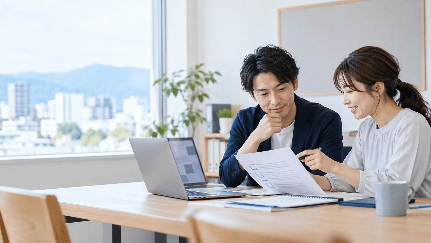 明るいオフィスで、二人の担当者がノートパソコンと更新手順のチェックリストを見ながら相談している様子